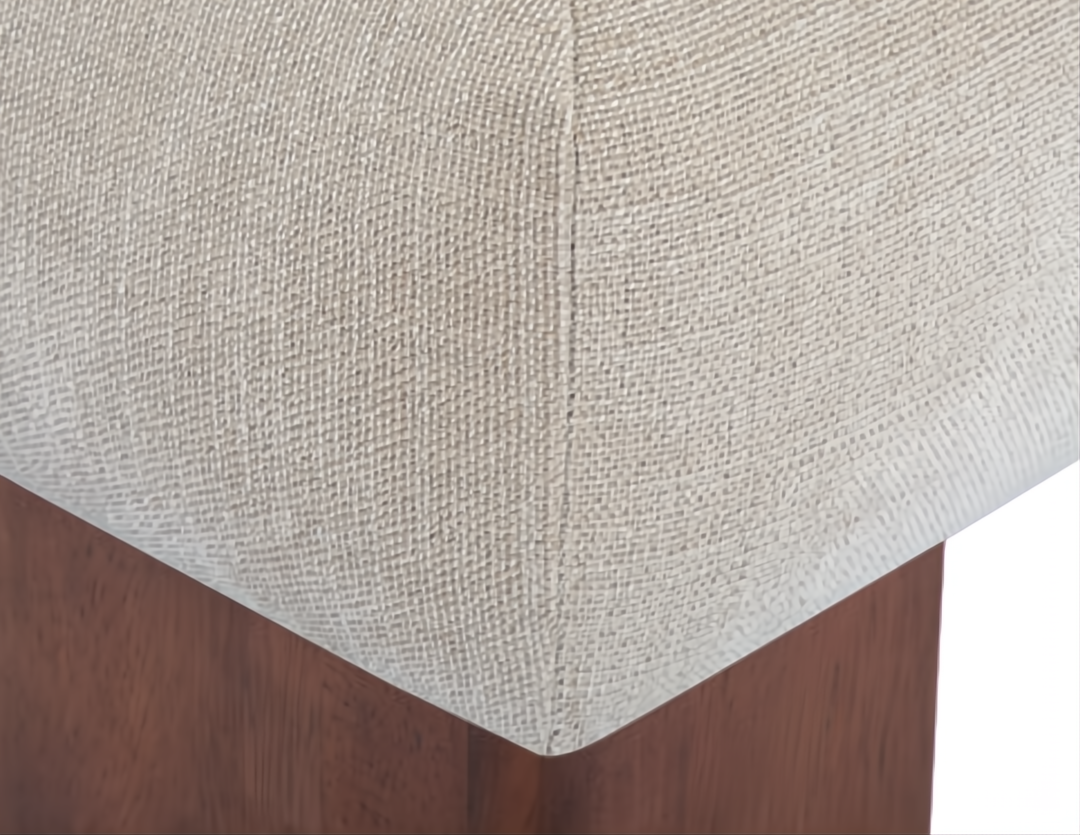 Close-up of a Surya Mirava Ottoman, showing the ivory polyester fabric and brown stained rubber wood base.