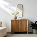Brown lacquered mango wood Surya Ronan Cabinet with vertical slat doors, a beige vase, and a gold mirror.