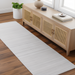 Light gray hand-loomed recycled PET yarn runner rug on a wood floor, complementing a natural wood cabinet.