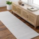 Light gray hand-loomed recycled PET yarn runner rug on a wood floor, complementing a natural wood cabinet.