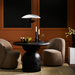 Surya Koben 39" round black mango wood dining table with sculptural base, flanked by two brown chairs.