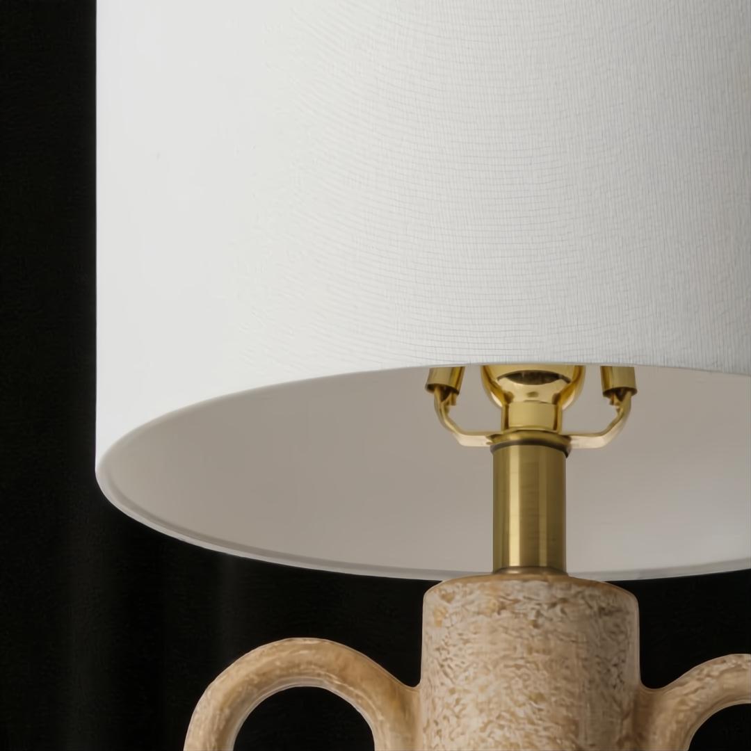 Surya Brava accent table lamp with a white fabric shade, brass hardware, and a textured beige base.