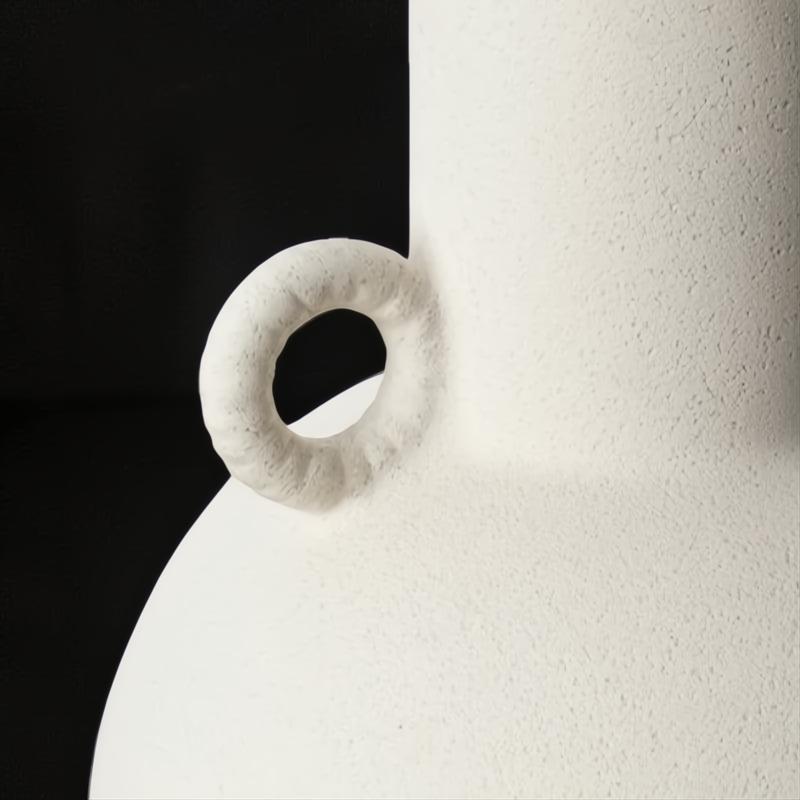 Close-up of a white textured ceramic decorative accent with a sculptural, vase-like form and a small ring handle.