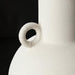 Close-up of a white textured ceramic decorative accent with a sculptural, vase-like form and a small ring handle.