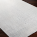 White, light blue, and light slate Surya Hope flatwoven rug made from recycled PET yarn on a dark wood floor.