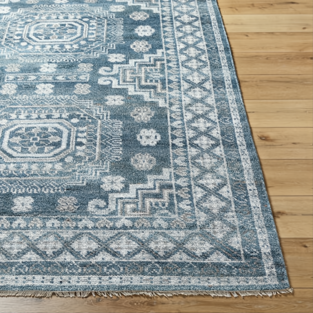 Surya Almeria low pile area rug with intricate geometric patterns in blue, gray, and cream, on a wood floor.