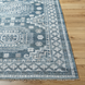 Surya Almeria low pile area rug with intricate geometric patterns in blue, gray, and cream, on a wood floor.