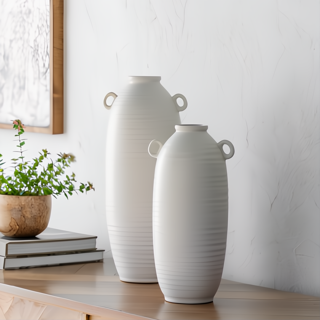 Two cream ceramic Surya Kushan decorative vases, one large and one small, with textured horizontal ridges and loop handles.