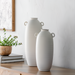Two cream ceramic Surya Kushan decorative vases, one large and one small, with textured horizontal ridges and loop handles.