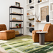 Two brown leather modular chairs with a black base, a green abstract rug, and white shelves.