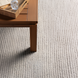 Surya Azalea AZA-2315 hand-woven rug, light beige recycled PET yarn, with a wooden table.
