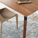 Dark brown oak veneer dining table with rubber wood and black metal base, shown with a beige chair on a patterned rug.