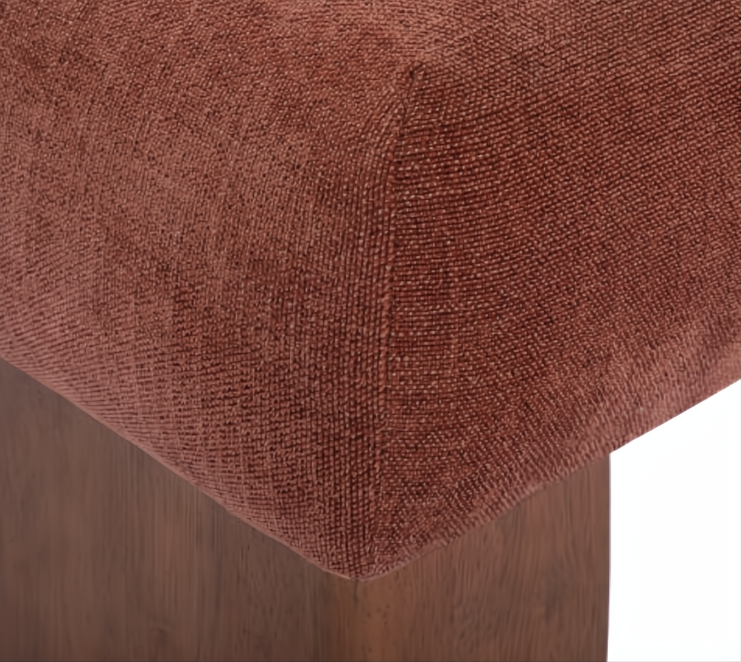 Close-up of a rust-colored upholstered ottoman with a textured polyester cover and dark wood base.