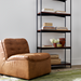 Brown leather modular chair with knife-edge design and black rubber wood base, beside a black metal bookshelf.
