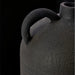 Close-up of a dark gray, textured ceramic decorative accent with a curved handle, against a black background.