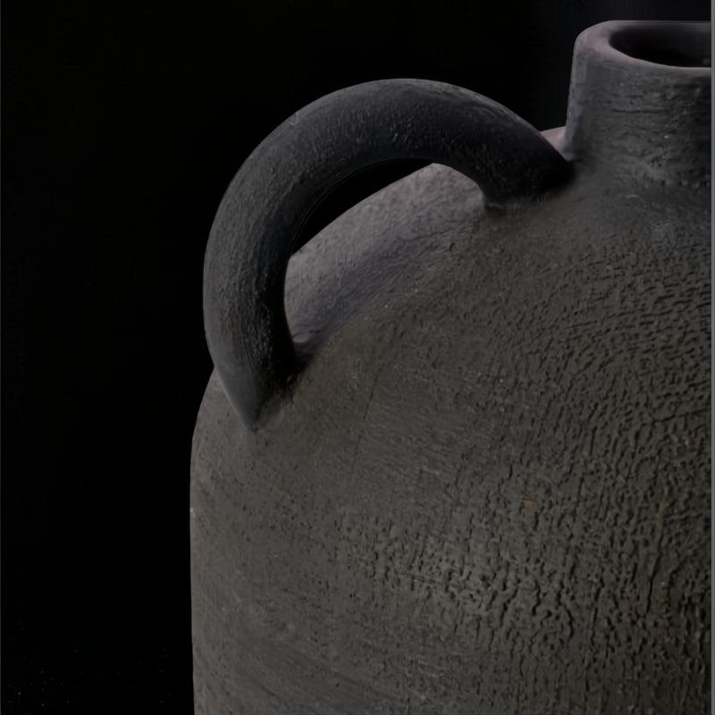 Close-up of a dark gray, textured ceramic decorative accent with a curved handle, against a black background.