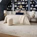 Cream bouclé Surya Mohave pouf in a farmhouse cottage bedroom with a beige bed and blue shelves.