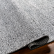 Hand-woven gray Surya Abby ABB-2300 area rug made from recycled PET yarn, partially rolled on a wood floor.