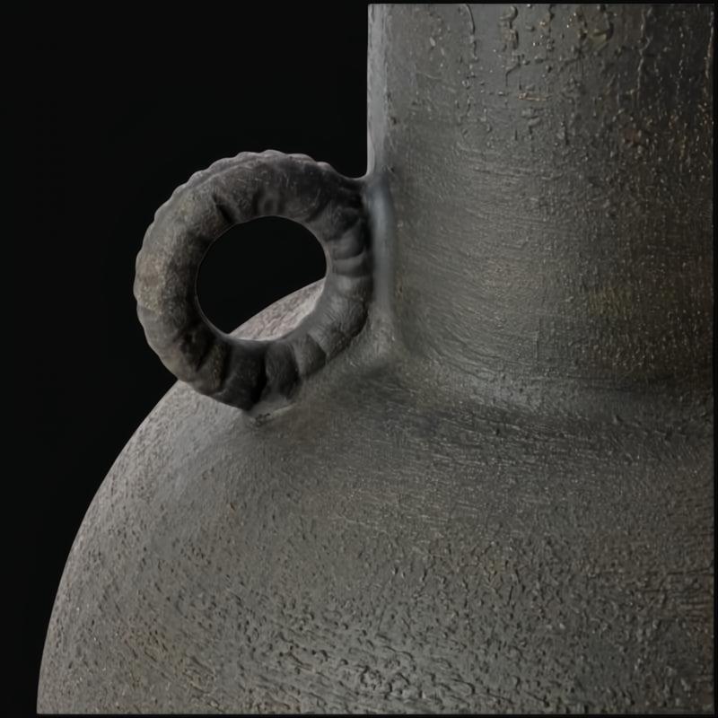Close-up of a dark, textured ceramic decorative accent with a sculptural, vase-like form and a ring handle.