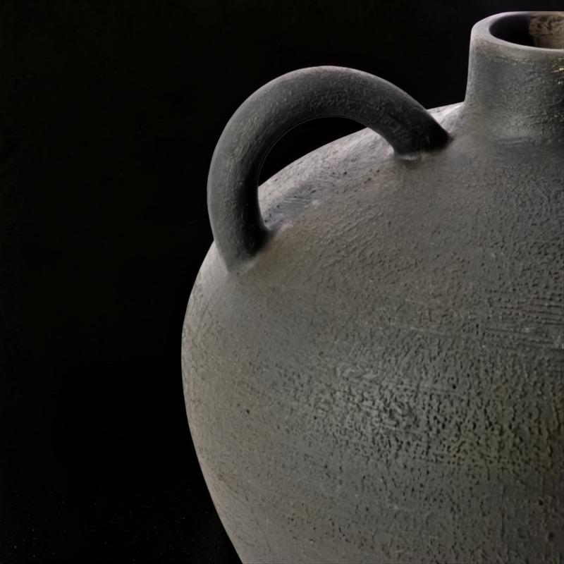 Close-up of a dark gray, textured ceramic decorative accent with a handle, against a black background.