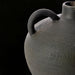 Close-up of a dark gray, textured ceramic decorative accent with a handle, against a black background.