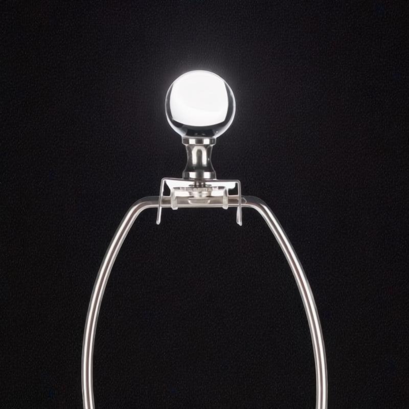 Silver metal lamp harp with a clear glass finial against a dark background.