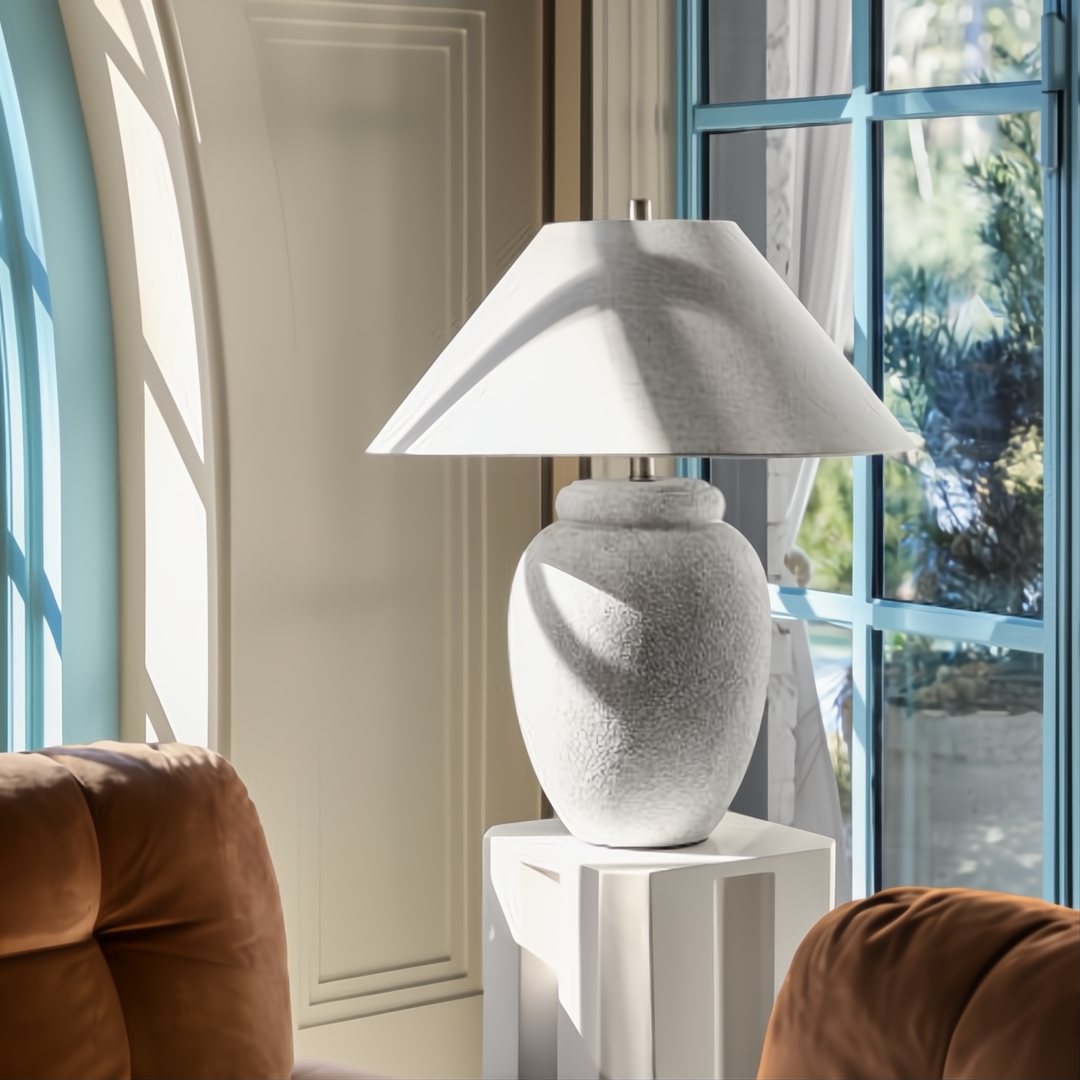 Surya Capelli accent table lamp with a textured white ceramic base and fabric shade, on a white pedestal.