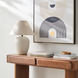 Surya Capelli accent table lamp with a cream ceramic base and fabric shade on a wooden console.