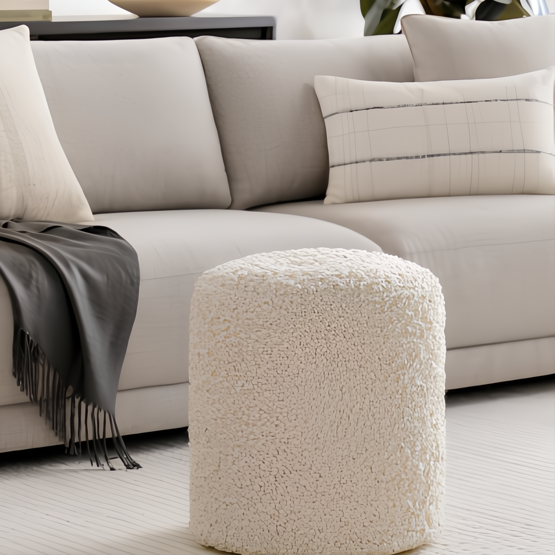 Cream bouclé Surya Mohave pouf, a cozy farmhouse cottage accent, in front of a light sofa.
