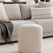 Cream bouclé Surya Mohave pouf, a cozy farmhouse cottage accent, in front of a light sofa.
