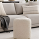 Cream bouclé Surya Mohave pouf, a cozy farmhouse cottage accent, in front of a light sofa.