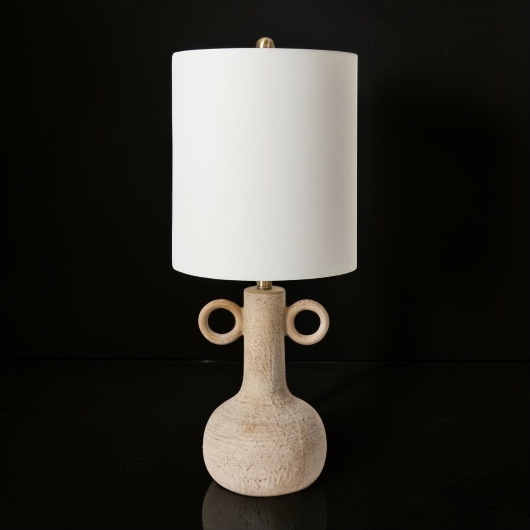 Surya Brava accent table lamp with a textured beige base, two ring handles, a white fabric shade, and gold accents.