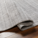 Surya Fresno FNO2302 hand-loomed rug in multi-tone gray recycled PET yarn, partially rolled on wood floor.