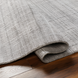 Surya Fresno FNO2302 hand-loomed rug in multi-tone gray recycled PET yarn, partially rolled on wood floor.