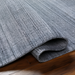 Surya Fresno FNO-2300-P hand-loomed rug in multi-gray recycled PET yarn, partially rolled on wood floor.