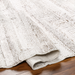 Hand-woven Surya Floria rug in neutral recycled PET yarn, partially rolled on a wood floor.