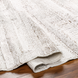 Hand-woven Surya Floria rug in neutral recycled PET yarn, partially rolled on a wood floor.