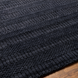 Surya Hickory HCK2300 area rug in charcoal, black, and gray with subtle textured patterning on a wood floor.
