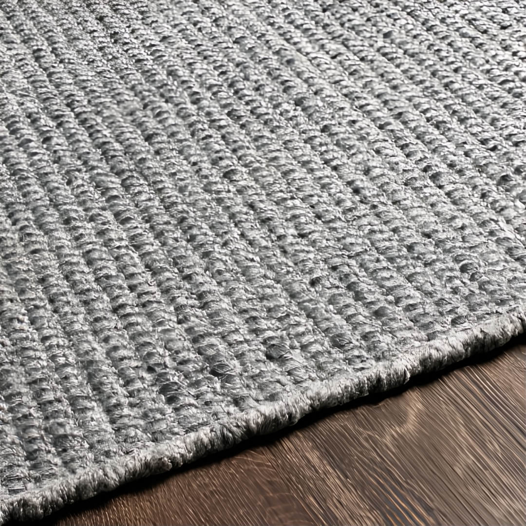 Close-up of a hand-woven, light gray Surya Azalea rug made from recycled PET yarn on a dark wood floor.