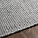 Close-up of a hand-woven, light gray Surya Azalea rug made from recycled PET yarn on a dark wood floor.