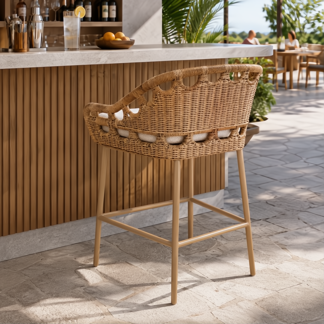 Woven rattan counter stool with light brown frame and white cushions, shown outdoors at a bar.