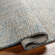 Surya Aiden AEN-1001 hand-tufted wool area rug in light blue and cream, partially rolled on a wood floor.