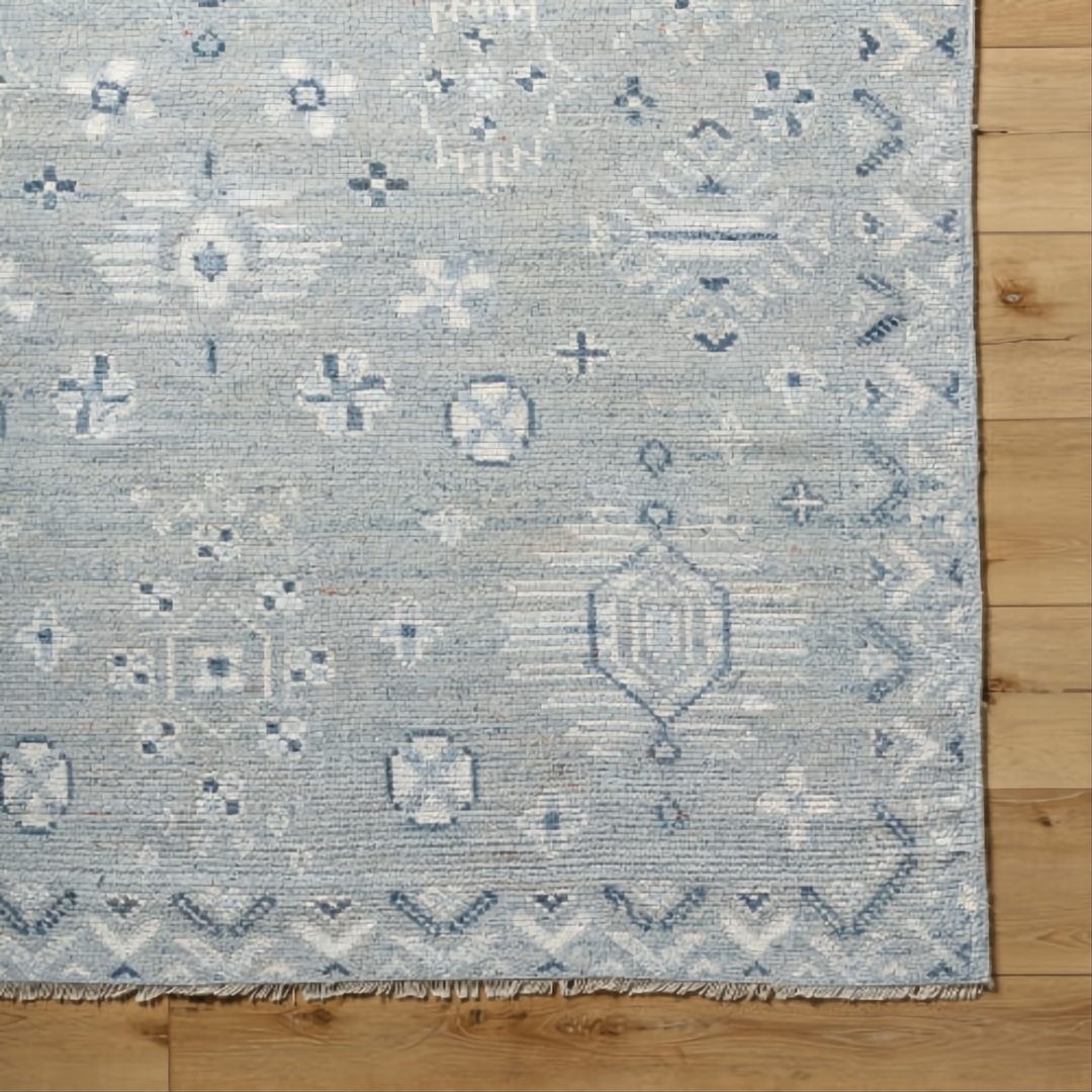 Hand-knotted Surya Almeria rug, low pile with light blue, white, and gray geometric patterns, fringe detail.