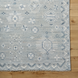 Hand-knotted Surya Almeria rug, low pile with light blue, white, and gray geometric patterns, fringe detail.