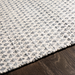 Close-up of Surya Azalea AZA-2306 rug, hand-woven from recycled PET yarn, featuring a subtle gray and white repeating pattern on dark wood.