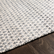 Close-up of Surya Azalea AZA-2306 rug, hand-woven from recycled PET yarn, featuring a subtle gray and white repeating pattern on dark wood.