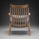 Rear view of a modern wooden accent chair with a slatted back and gray herringbone cushions.