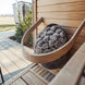Huum Drop 9KW sauna heater add-on, a sleek metal basket filled with gray stones, mounted on light wood paneling.