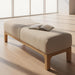 Light beige polyester Bradly Bench with a beige stained red oak base and an open magazine on top.