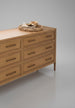 Wide brown painted oak veneer dresser with six soft-close drawers, brass pulls, and a woven tray on top.